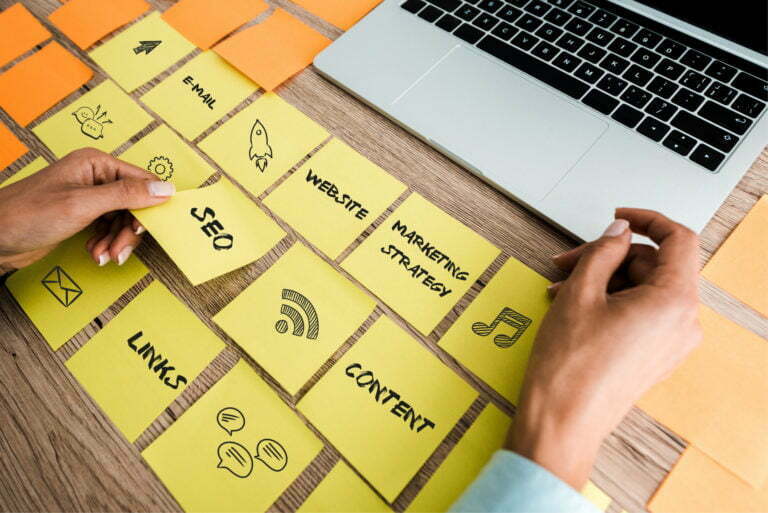 cropped view of woman touching sticky note with seo lettering near laptop on desk